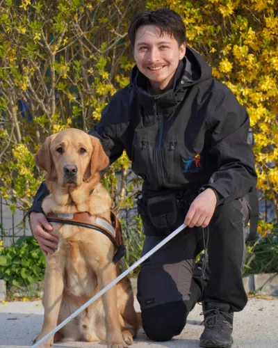 Photo de Kaelig, moniteur à l'éducation avec son chien, un labrador de couleur sable portant son body de travail.