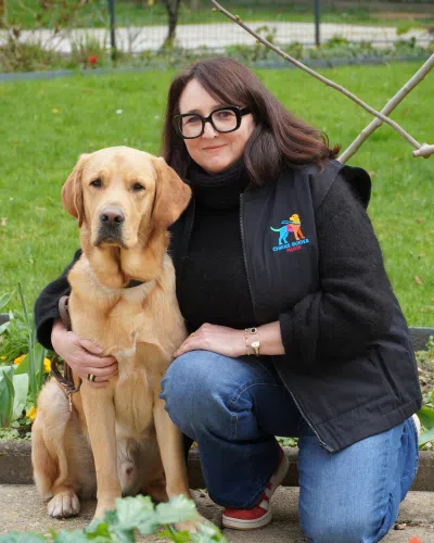 Photo de Catherine, comptable portant son gilet de l'Ecole avec un chien de couleur sable à sa gauche