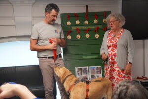 Photo de Stanislas, référent retraite, remettant une médaille à un chien guide retraité de couleur sable. La médaille est dorée et suspendue à un cordon rouge.
