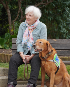 Photo d'Anne, famille de retraite, et de Monroy, chien guide retraité. Tous deux sont assis, et la photo est prise en extérieur.