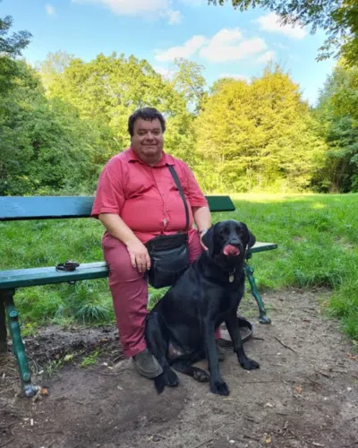 Dominique Lemaître est assis sur un banc, Pessos, son chien guide est entre ses jambes