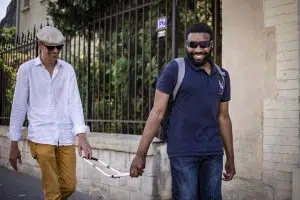 Dimitri, inspecteur en locomotion pris en photo lors d'une séance en extérieur, avec derrière lui une personne mal voyante