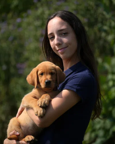 Photo de Zoe , technicienne d’élevage à Buc, tenant dans ses bras un chiot roux.