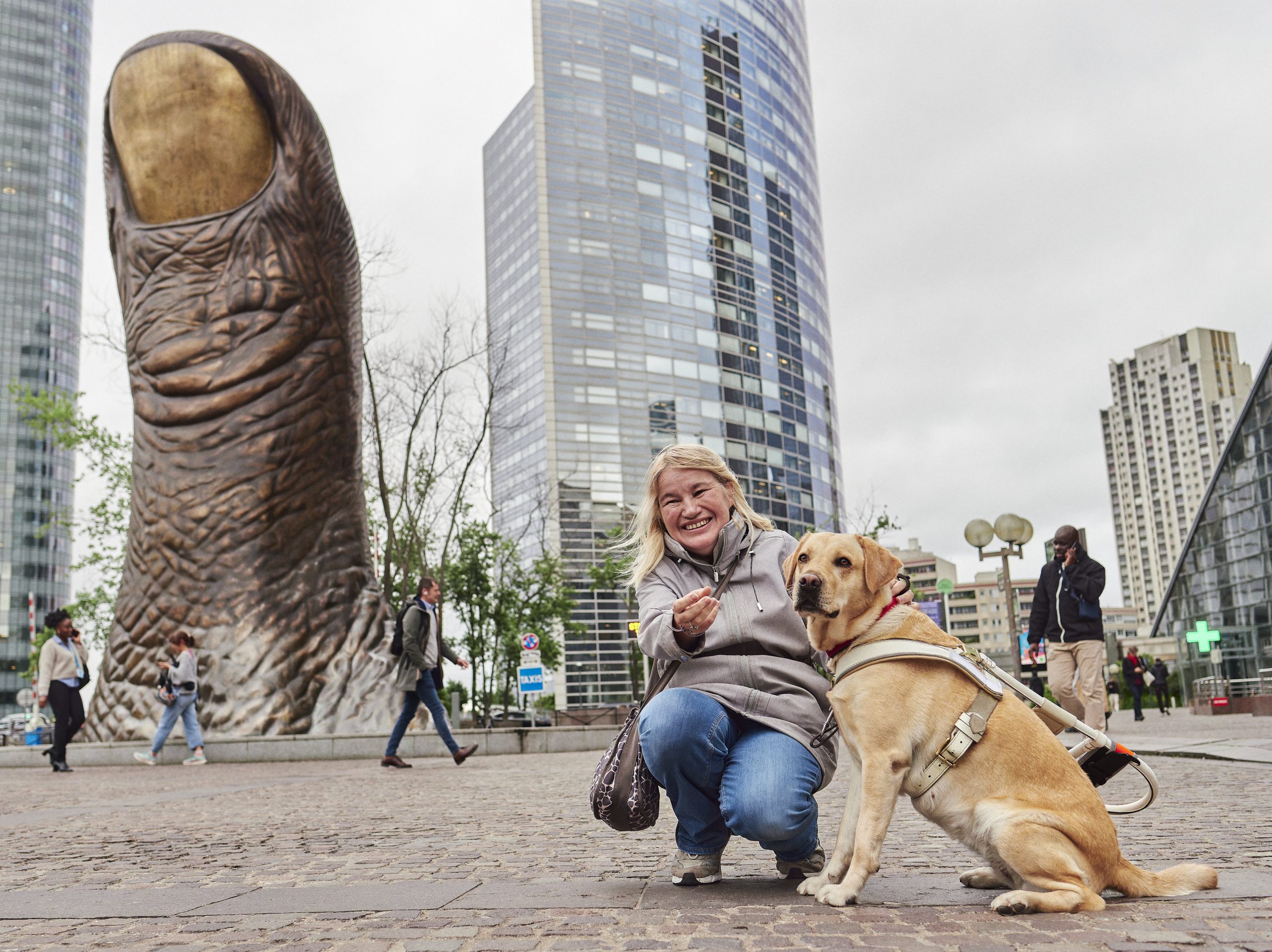 Photo de Corine, une bénéficiaire, et de Rose, sa chienne labrador, photographiées sur le parvis de La Défense, l’endroit où Corine travaille.