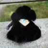 Photo d'une peluche noir fluffy assise de dos , pour montrer le logo de l'Ecole cousu sur le bandana