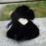 Photo d'une peluche noir fluffy assise de dos , pour montrer le logo de l'Ecole cousu sur le bandana