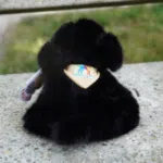 Photo d'une peluche noir fluffy assise de dos , pour montrer le logo de l'Ecole cousu sur le bandana